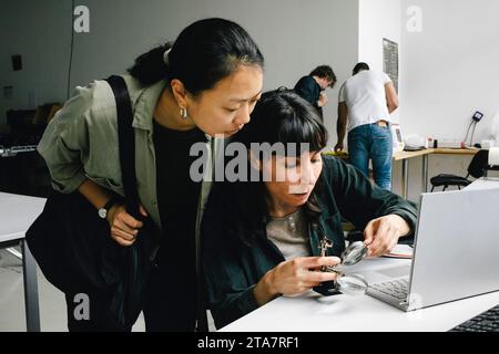 Customer standing near focused female technician examining laptop through magnifying glass at repair shop Stock Photo