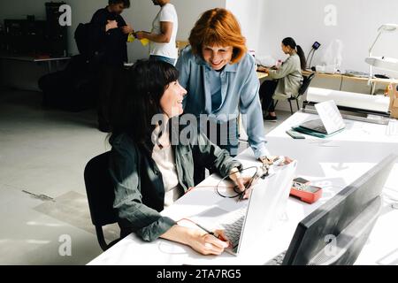 Smiling senior woman discussing with female technician repairing laptop at repair shop Stock Photo