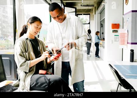 Smiling male and female technicians examining machine parts using multimeter at repair shop Stock Photo