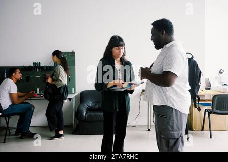 Side view of young male customer discussing with female technician holding laptop at repair shop Stock Photo