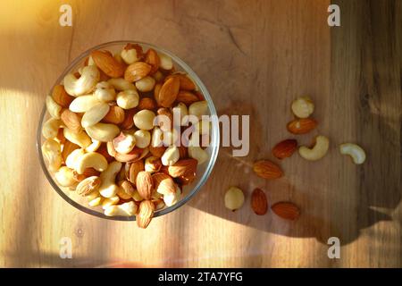 Cashews, peanuts and almonds on a plate. Nuts on the table in the bright rays of the sun.. Stock Photo