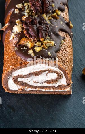 On a wooden board, a Swiss roll with hazelnuts, buttercream filling, and dark chocolate topping. This is perfect for any day or New Year's treats. Stock Photo