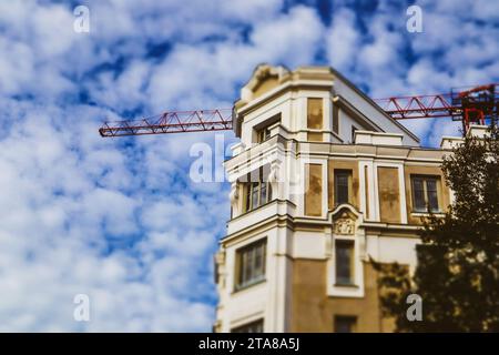 An old beige house, apartment building under construction Crane machine blue sky Stock Photo