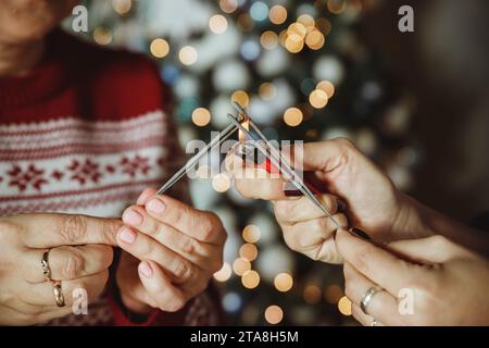Hands holding fireworks against christmas lights in dark room. Happy New Year. Atmospheric holiday. Friends celebrating with burning sparklers in Stock Photo