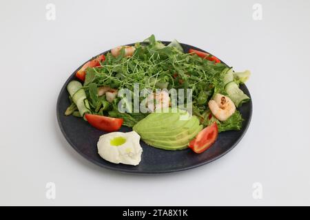 Shrimps salad, avocado, lettuce and cherry tomatoes. Tasty veg mixed leaves with grilled prawn shrimps in black plate on white background. Stock Photo