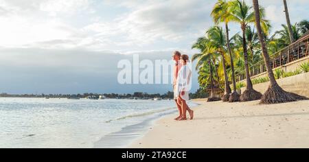 Couple in love hugging on sandy exotic beach while having evening walk by Trou-aux-Biches seashore on Mauritius island enjoying sunset. People relatio Stock Photo