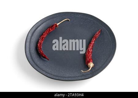 Empty dark ceramic plate framed with dry hot capsicums isolated on a white background. Top view with copy space Stock Photo