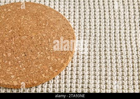 A fragment of a round beige cork coaster on a rough knitted tablecloth. Food menu template Stock Photo