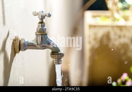 Open water tap in the backyard. Open faucet with water running. Waste of drinking water. Responsible use of water concept. Stock Photo