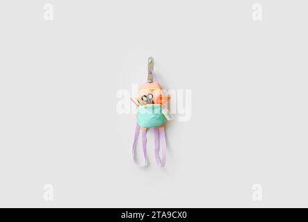 Stylish backpack with different stationery hanging on light wall Stock Photo