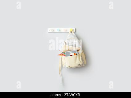 Stylish school backpack with stationery hanging on light wall Stock Photo