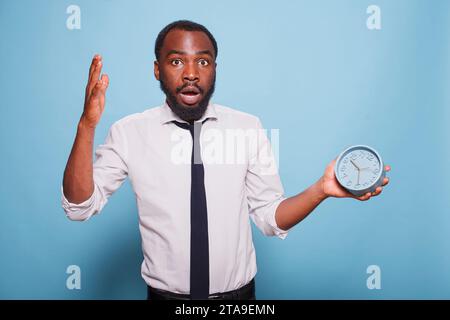 African American male entrepreneur shockingly looking at clock before going for company meeting. Black businessman appears to be in a panic, rushing and experiencing an emergency. Stock Photo