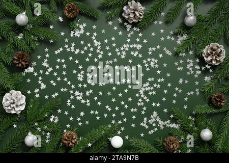 Christmas frame with fir branches, cones and silver decorations on a green background. New Year greeting card with copy space. Top view, flat lay. Stock Photo
