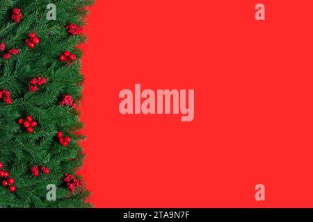 Christmas border with fir branches and red berries. Christmas red background. New Year card. Festive greeting card with space for text. Top view, flat Stock Photo