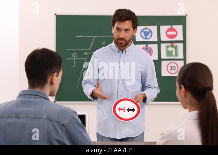 Teacher showing No Overtaking road sign during lesson in driving school Stock Photo