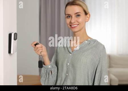 Home security system. Smiling woman using alarm key fob in room Stock Photo
