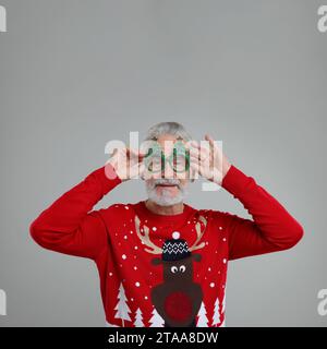 Senior man in Christmas sweater and funny glasses on grey background Stock Photo