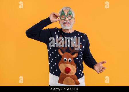 Senior man in Christmas sweater and funny glasses against orange background Stock Photo
