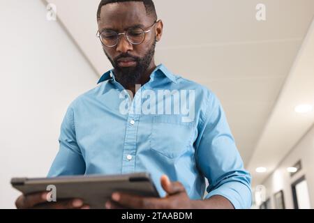 African american male doctor using tablet in corridor in hospital Stock Photo