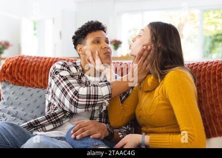 Portrait of happy diverse couple sitting on couch and making funny faces at home, copy space. Expression, leisure, love, togetherness, gesticulation, Stock Photo