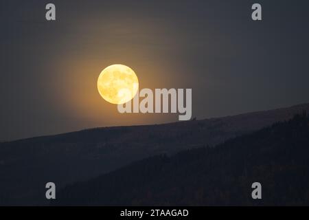 Mist gives a soft glow to the Full Beaver moon rising behind mountain ridge Stock Photo