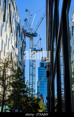 Two tower cranes on a construction site seen between buildings on Jack Rosenthal Street, First Street district, Manchester, England, UK Stock Photo