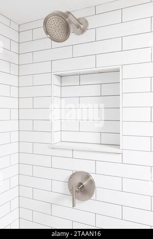 A bathroom shower detail with white subway tile walls, a built-in niche shelf, and a bronze shower head. Stock Photo