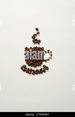 On the white background, brown roasted coffee beans arranged in the shape of a cup of coffee with hot smoke rising from it. Creative background for ad Stock Photo