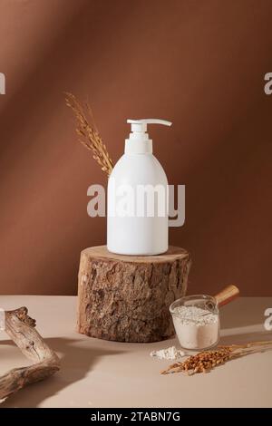 An unlabeled bottle of shower gel is displayed on a log. Rice bran powder is stored in a glass bowl. Minimalist brown background for product advertisi Stock Photo