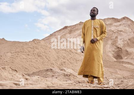 Wide angle shot of young Black man wearing traditional kaftan in desert landscape, copy space Stock Photo