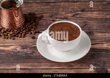 Double Turkish coffee in a white porcelain cup with a decorative coffee pot on a wooden table Stock Photo