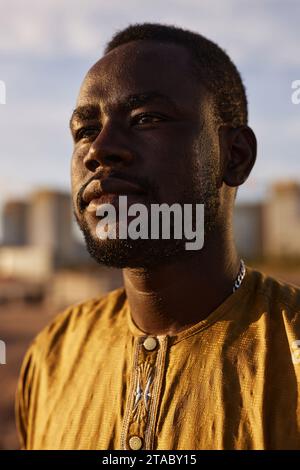 Dramatic portrait of Black young man looking away in half shadow outdoors Stock Photo