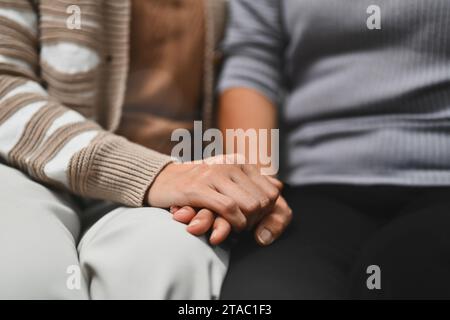 Grown up daughter holding hands of old mother for giving support, empathy and understanding Stock Photo