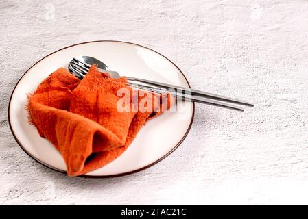 White empty plate with cutlery on orange textile napkin. Autumn table setting. Top view Stock Photo