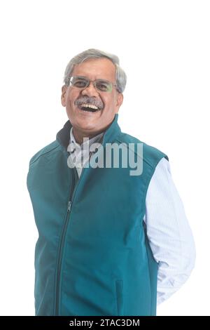 A smiling senior Indian businessman or executive with grey hair in a light blue shirt and sleveless jacket isolated on white Stock Photo
