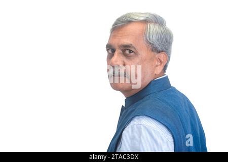 A smiling senior Indian businessman or executive with grey hair in a light blue shirt and sleveless jacket isolated on white Stock Photo