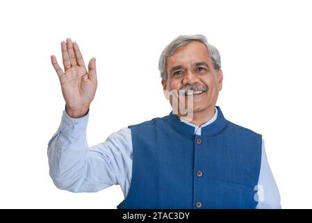 A smiling senior Indian businessman or executive with grey hair in a light blue shirt and sleveless jacket waving isolated on white Stock Photo