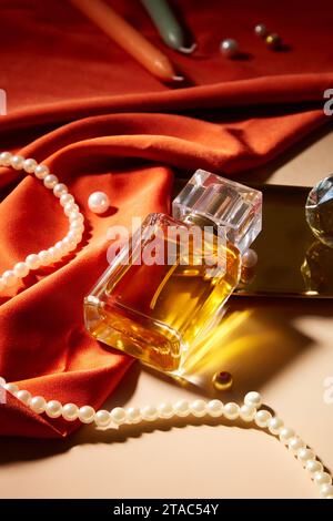 A bottle of perfume without label is displayed on a table with a string of pearls, candles and red silk. Mockup for perfume advertisement with blank l Stock Photo