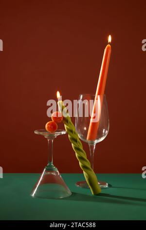 Two burning candles are placed next to a cocktail glass and a wine glass on a deep green and brown background. Mysterious space for advertising and so Stock Photo