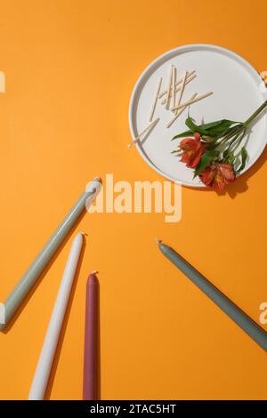 A flower branch and matchsticks are placed on a white ceramic plate. The candles are placed randomly on a yellow background. Candles are used for ligh Stock Photo