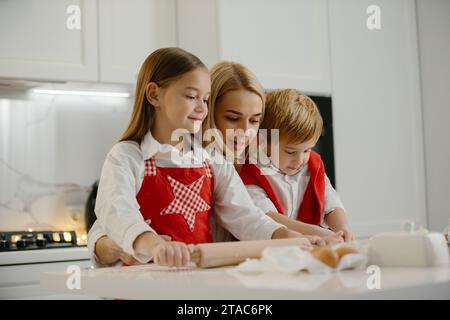 Christmas, mother and children are making cookies in the kitchen. Mother teaches children to bake cookies. Stock Photo
