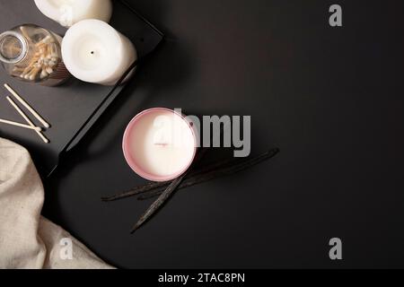 Two white candles and a bottle of cotton swabs are displayed on a black tray. A jar of scented candles is placed on the table with a black background. Stock Photo