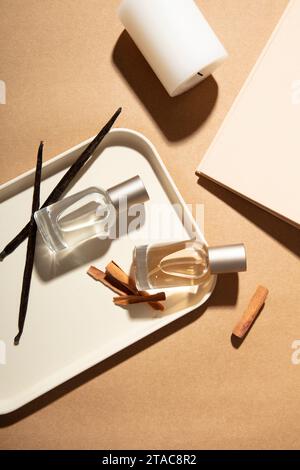 Two unlabeled perfume bottles are placed on a tray with cinnamon. On the table there is a horizontal white candle. Pastel brown background with mockup Stock Photo