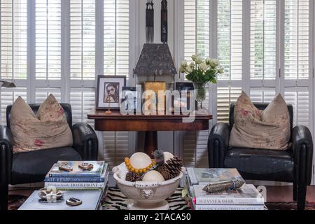 Rosewood table and worn leather armchairs with closed shutters in single-storey colonial style home.Truro, Cornwall, UK. Stock Photo