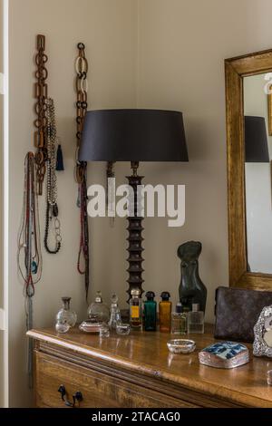 Lamp and perfume with necklaces on dressing table in colonial style single-storey home. Truro, Cornwall, UK. Stock Photo