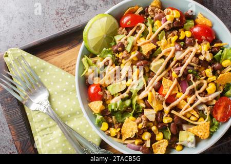 Beef Taco Salad made with beans, corn, nacho chips, lettuce, tomato, onion, cheese and avocado closeup on the plate on the table. Horizontal top view Stock Photo