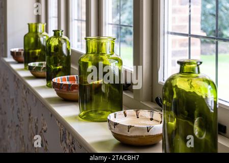 Large green bottles and ceramic bowls on windowsill in 1930s Arts and Crafts style home. Hove, East Sussex, UK. Stock Photo