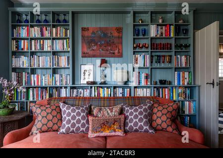 Blue tongue and groove book shelves with orange sofa in 1930s Arts and Crafts style home. Hove, East Sussex, UK. Stock Photo