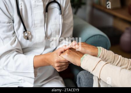 Close up of supportive female caregiver hold hand of mature grandmother visit patient at home, caring woman doctor support old senior grandma give con Stock Photo