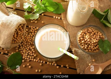 Glass of natural soy drink on wooden table with bowls full of seeds in the field. Top view. Stock Photo